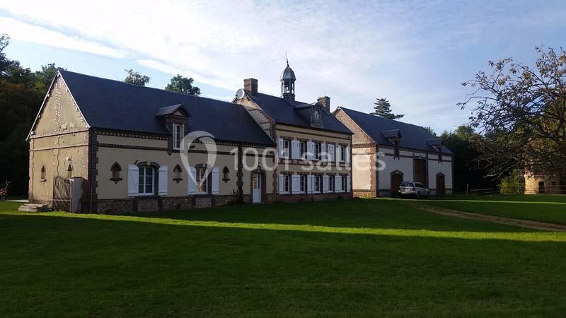 Location salle Sylvains-les-Moulins (Eure) - Domaine de Coulonge #13 Bâtiment ancien avec façade en pierre et toit d'ardoise, entouré d'une pelouse et d'arbres sous un ciel dégagé.