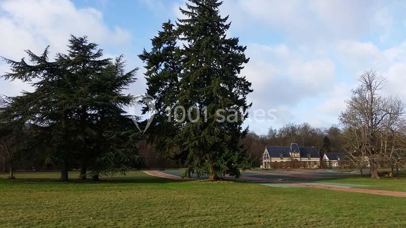 Location salle Sylvains-les-Moulins (Eure) - Domaine de Coulonge #32 Grand parc avec pelouse, allées pavées, arbres imposants et une maison en arrière-plan sous un ciel partiellement nuageux.