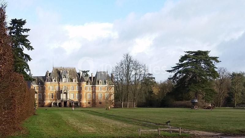 Location salle Sylvains-les-Moulins (Eure) - Domaine de Coulonge #31 Château en briques rouges entouré de pelouses, d'arbres et d'un ciel partiellement nuageux.