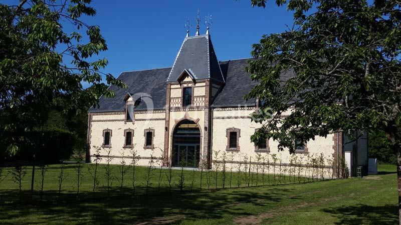 Location salle Sylvains-les-Moulins (Eure) - Domaine de Coulonge #4 Bâtiment en briques claires avec toit en ardoise, entouré de pelouse et d'arbres sous un ciel bleu.