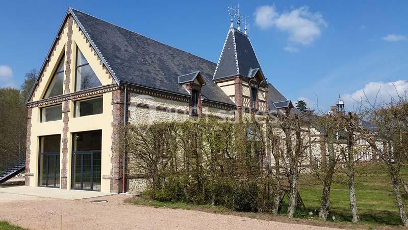Location salle Sylvains-les-Moulins (Eure) - Domaine de Coulonge #6 Bâtiment en pierre et brique avec toit en ardoise, entouré d'arbustes et situé dans un environnement verdoyant.