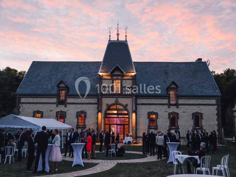 Location salle Sylvains-les-Moulins (Eure) - Domaine de Coulonge #7 Groupe de personnes rassemblées devant un bâtiment ancien avec toit en ardoise, au coucher du soleil.