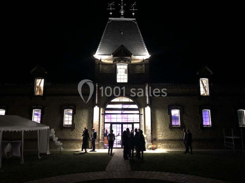 Location salle Sylvains-les-Moulins (Eure) - Domaine de Coulonge #10 Façade d'un bâtiment éclairé de nuit, avec des silhouettes de personnes devant l'entrée principale.