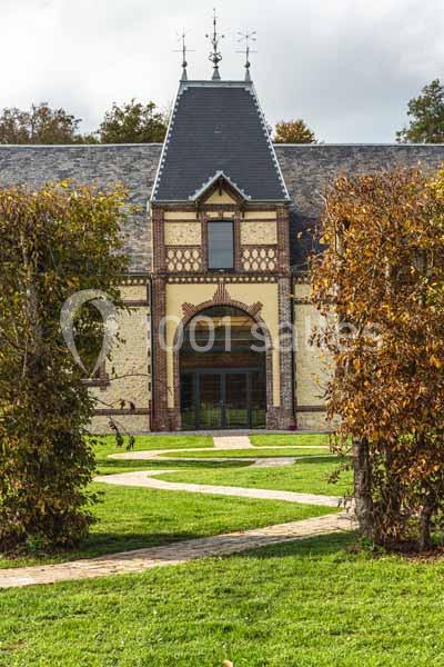 Location salle Sylvains-les-Moulins (Eure) - Domaine de Coulonge #2 Façade d'un bâtiment en briques avec toit en ardoise, vue à travers une allée bordée de haies taillées.