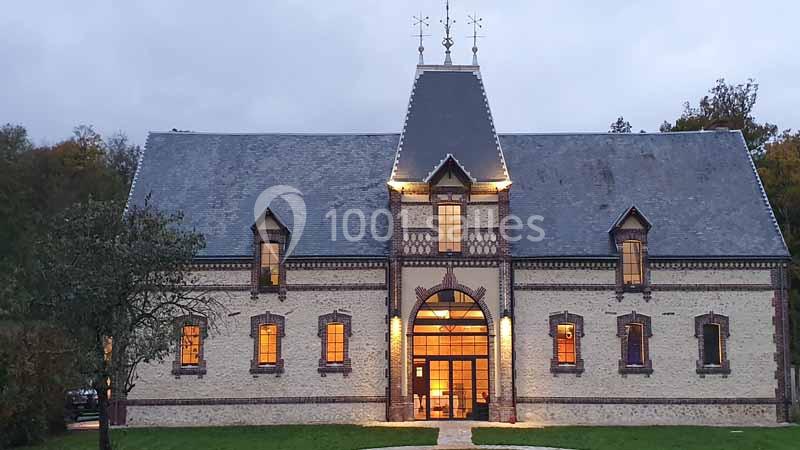Location salle Sylvains-les-Moulins (Eure) - Domaine de Coulonge #3 Façade d'un bâtiment en briques et pierre avec toit en ardoise, éclairé à la tombée de la nuit.
