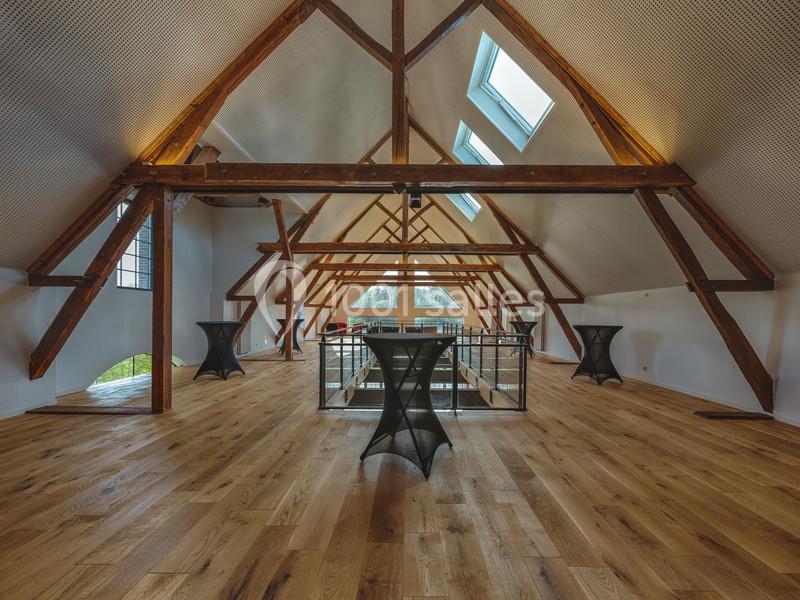 Location salle Sylvains-les-Moulins (Eure) - Domaine de Coulonge #24 Grande pièce sous combles avec poutres apparentes, parquet en bois clair, tables hautes et puits de lumière.