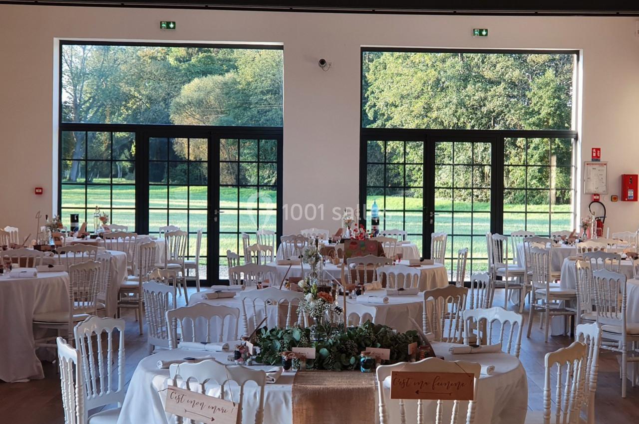 Location salle Sylvains-les-Moulins (Eure) - Domaine de Coulonge #22 Salle de réception lumineuse avec tables décorées, grandes baies vitrées donnant sur un parc verdoyant.
