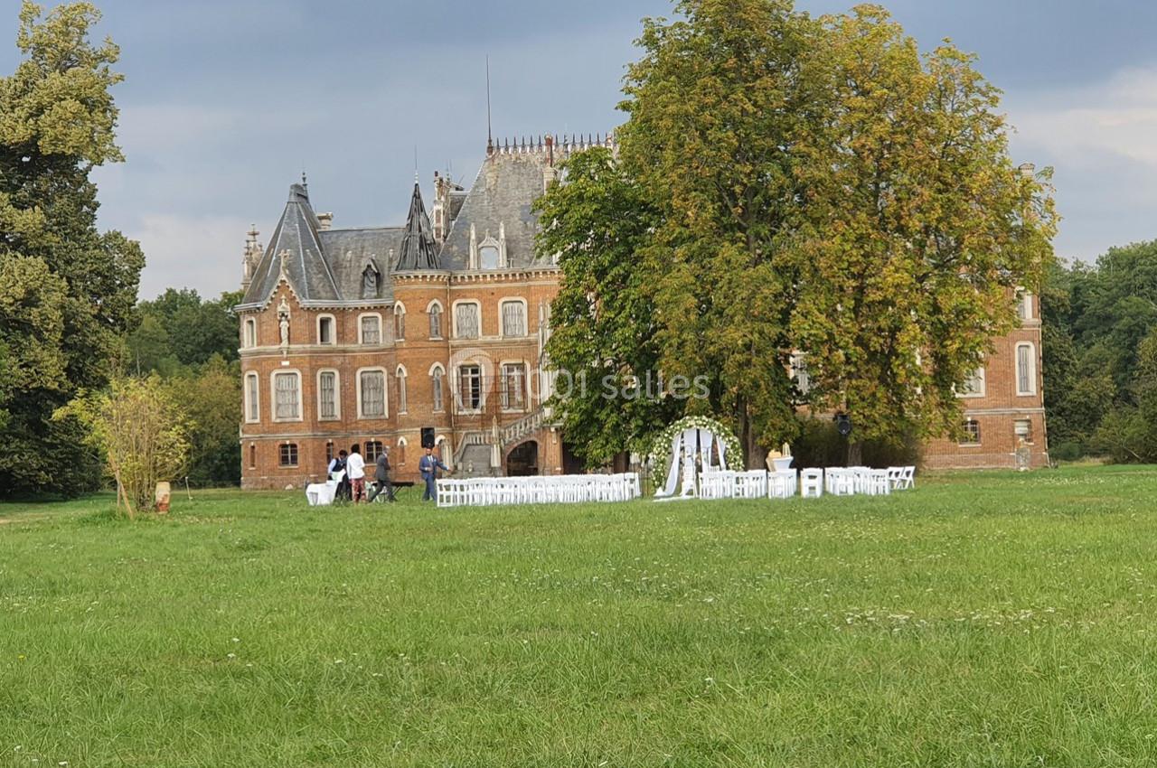 Location salle Sylvains-les-Moulins (Eure) - Domaine de Coulonge #27 Château en briques entouré de verdure avec des chaises blanches disposées pour une cérémonie en plein air.