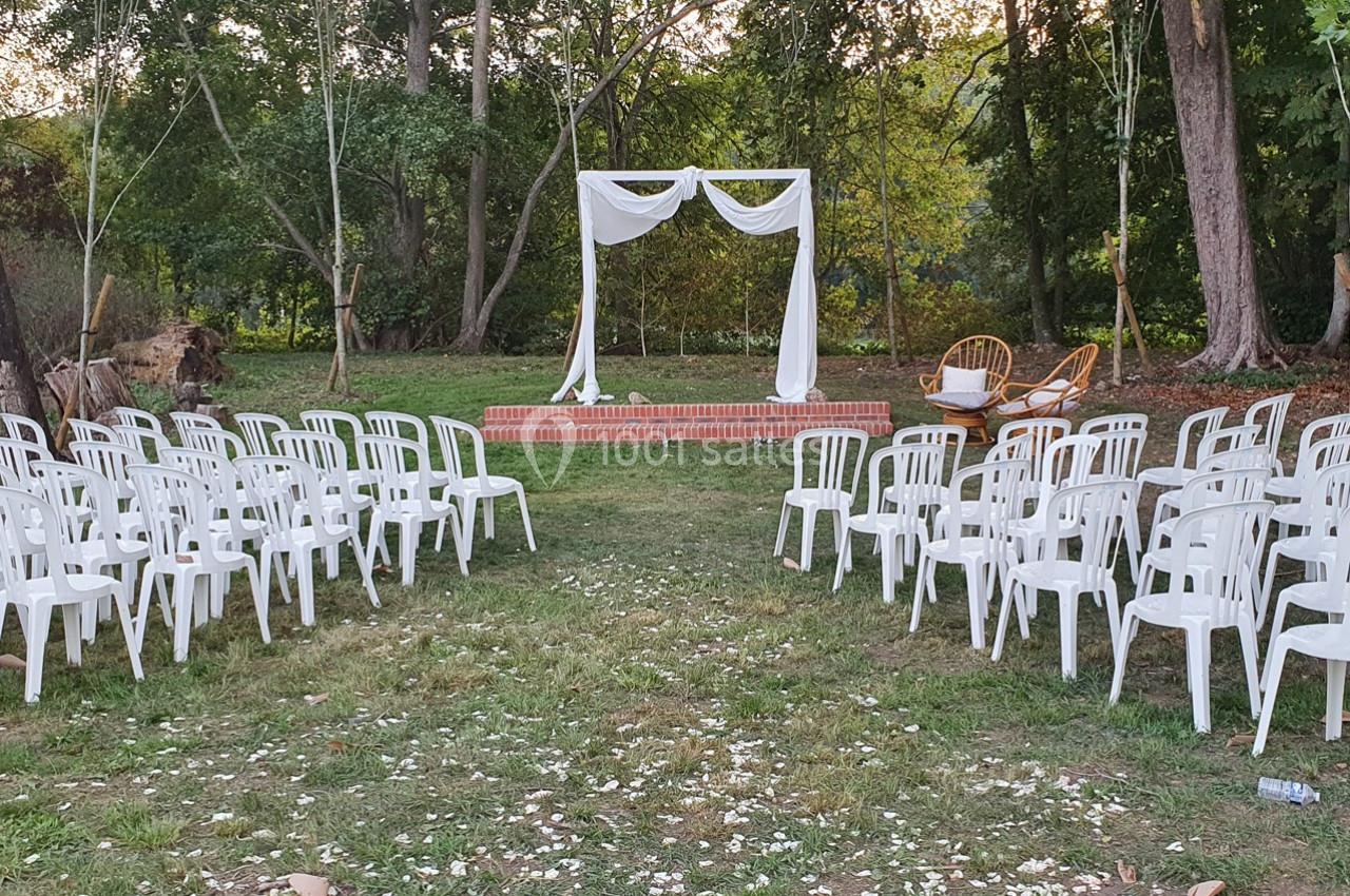 Location salle Sylvains-les-Moulins (Eure) - Domaine de Coulonge #30 Chaises blanches disposées en rangées devant une arche décorée de tissu blanc dans un cadre extérieur boisé.