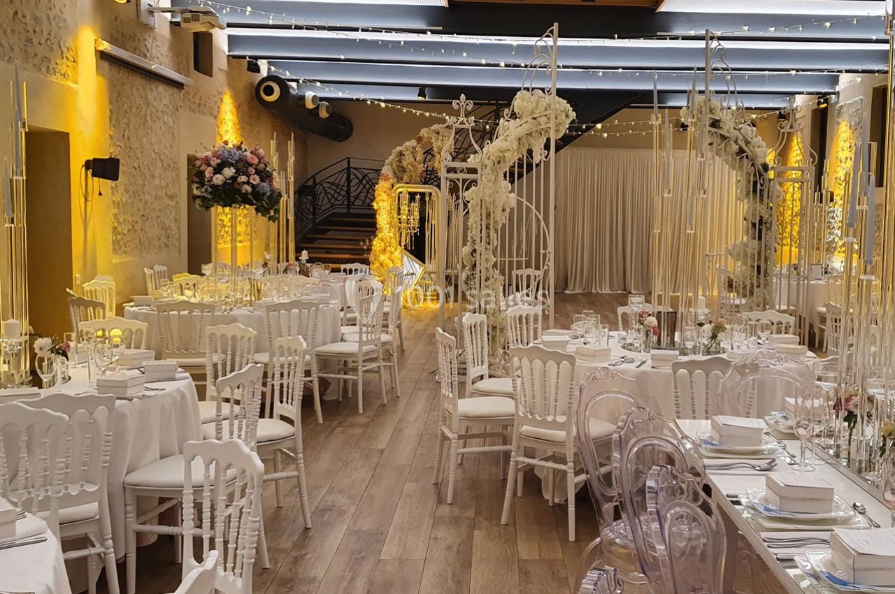 Location salle Sylvains-les-Moulins (Eure) - Domaine de Coulonge #21 Salle de réception décorée pour un mariage, avec tables dressées, chaises blanches et arches ornées de fleurs.