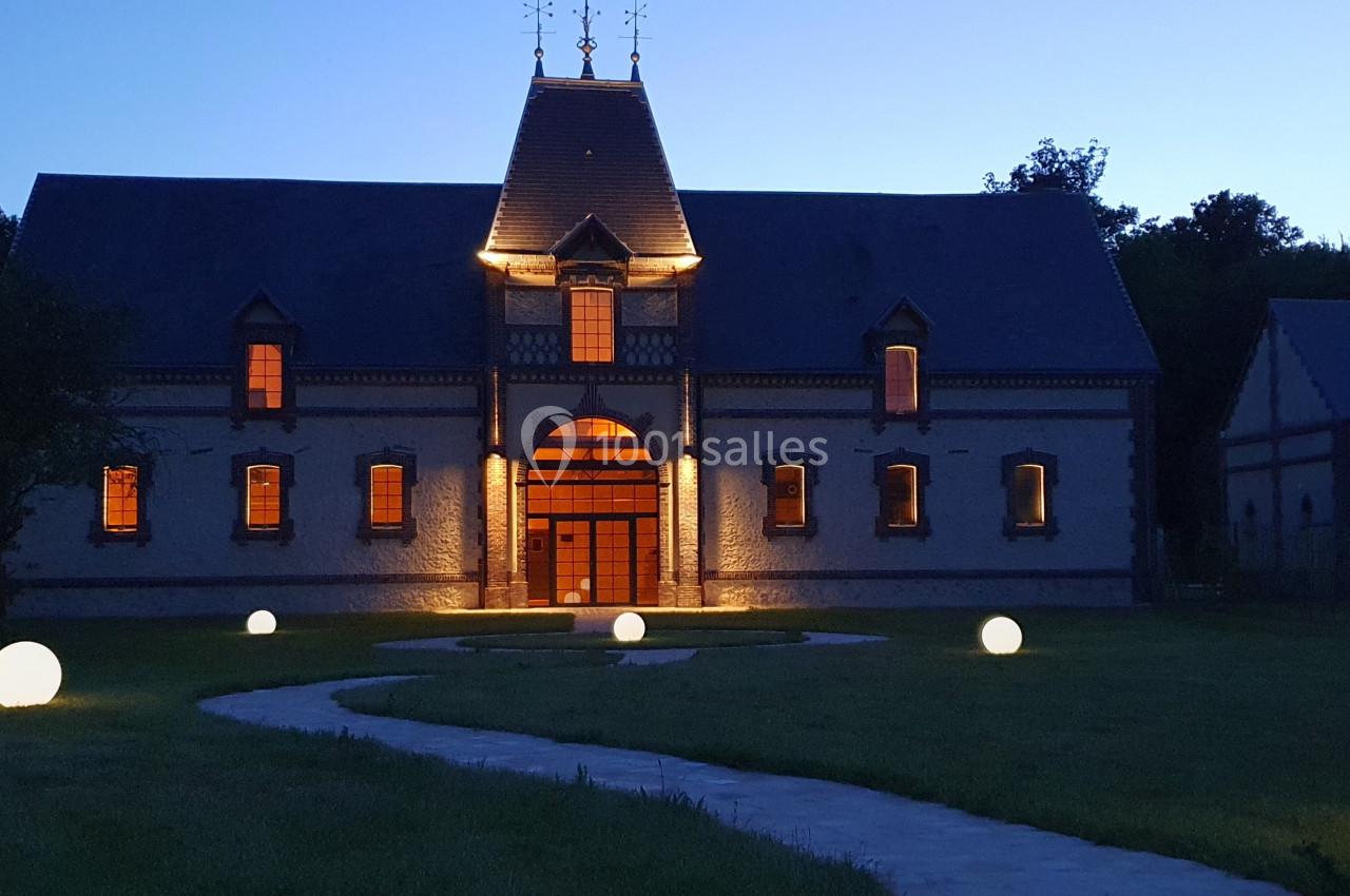 Location salle Sylvains-les-Moulins (Eure) - Domaine de Coulonge #12 Bâtiment en briques éclairé à la tombée de la nuit, avec un chemin bordé de sphères lumineuses dans un jardin.