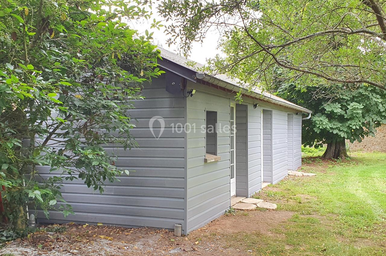 Location salle Sylvains-les-Moulins (Eure) - Domaine de Coulonge #33 Abri de jardin en bois gris clair avec fenêtres, entouré d'arbres et d'une pelouse verdoyante.