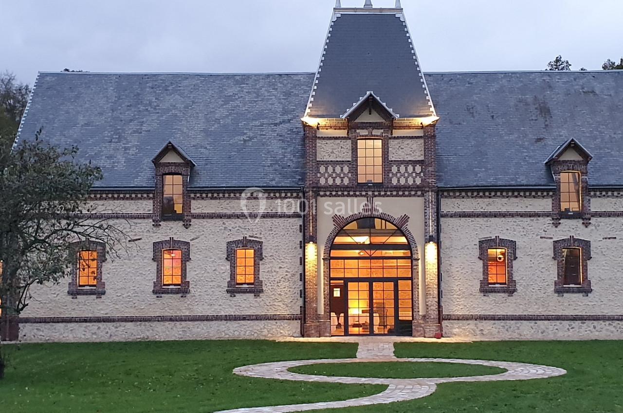 Location salle Sylvains-les-Moulins (Eure) - Domaine de Coulonge #8 Façade d'un bâtiment en briques avec toit en ardoise, éclairé à la tombée de la nuit, entouré de pelouse.