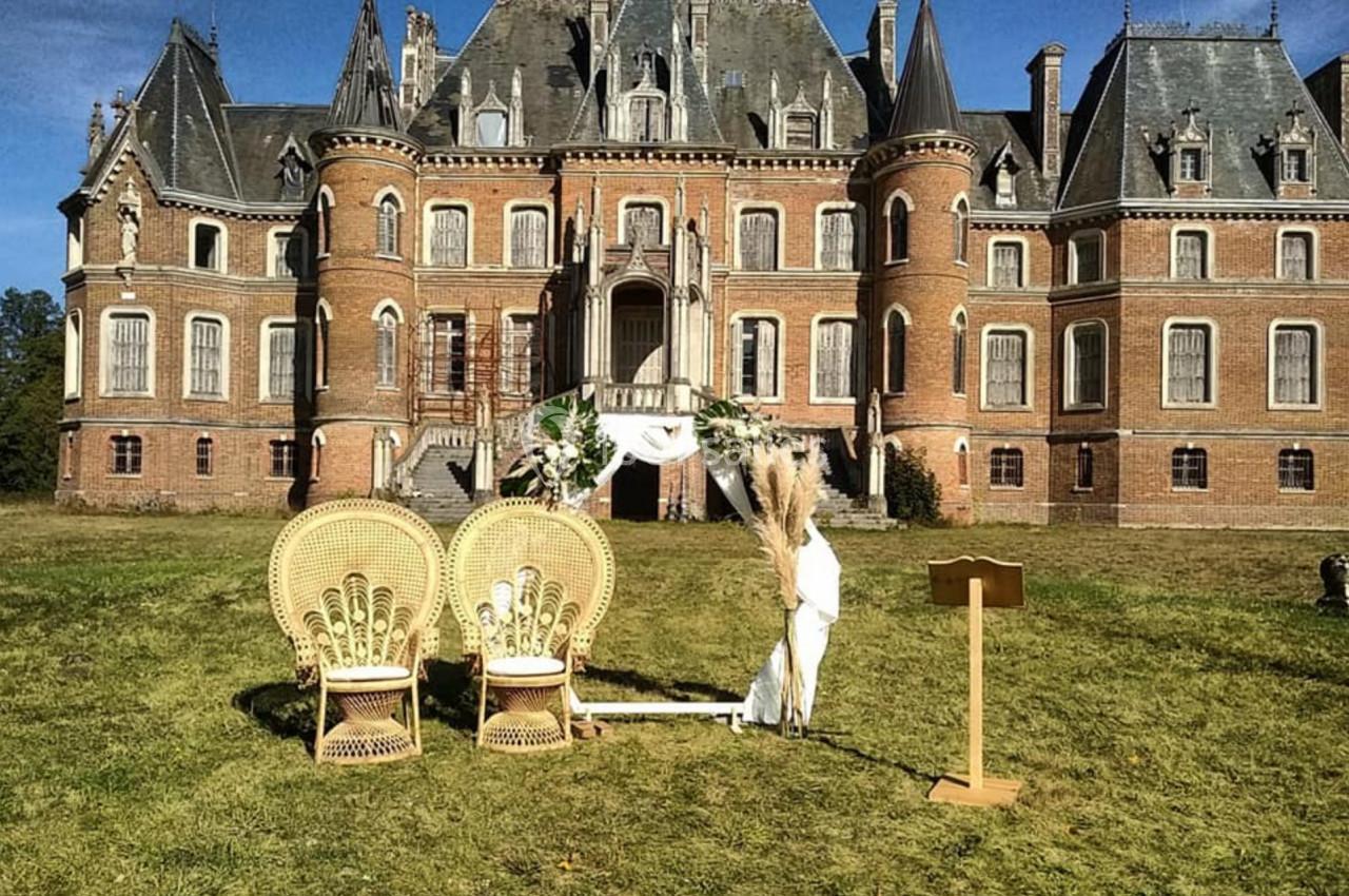 Location salle Sylvains-les-Moulins (Eure) - Domaine de Coulonge #29 Deux fauteuils en osier et une arche décorée devant un château en briques rouges sous un ciel bleu.