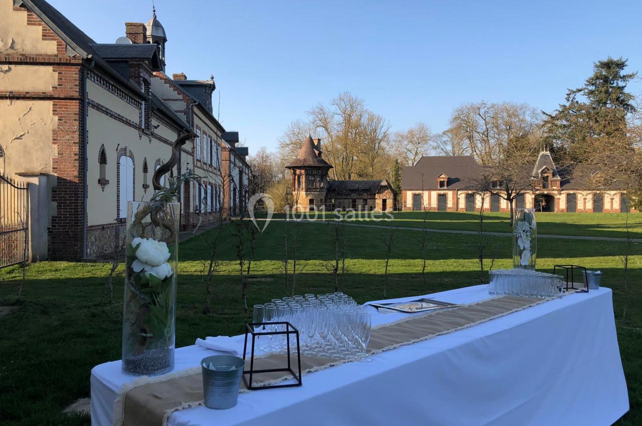 Location salle Sylvains-les-Moulins (Eure) - Domaine de Coulonge #34 Table dressée avec des verres et des décorations florales devant un bâtiment en briques dans un cadre verdoyant.