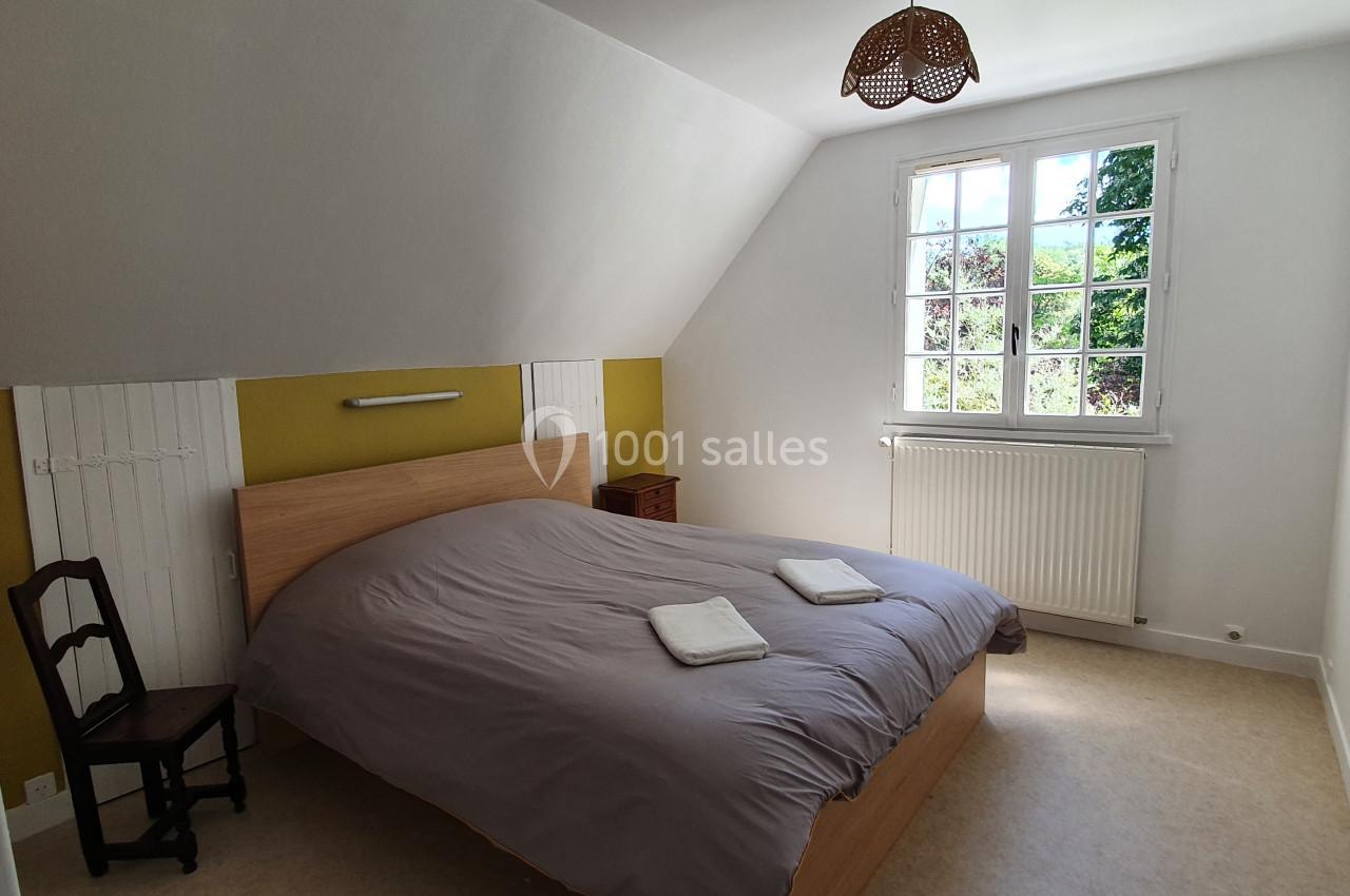 Location salle Sylvains-les-Moulins (Eure) - Domaine de Coulonge #37 Chambre lumineuse avec un lit double, deux serviettes pliées, une fenêtre donnant sur un jardin et un fauteuil en bois.