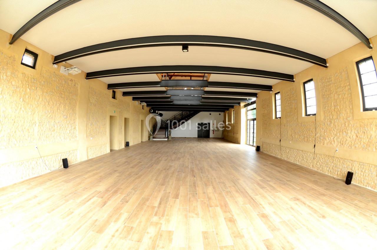 Location salle Sylvains-les-Moulins (Eure) - Domaine de Coulonge #16 Salle spacieuse avec parquet en bois, murs en pierre et poutres apparentes, éclairée par des fenêtres latérales.