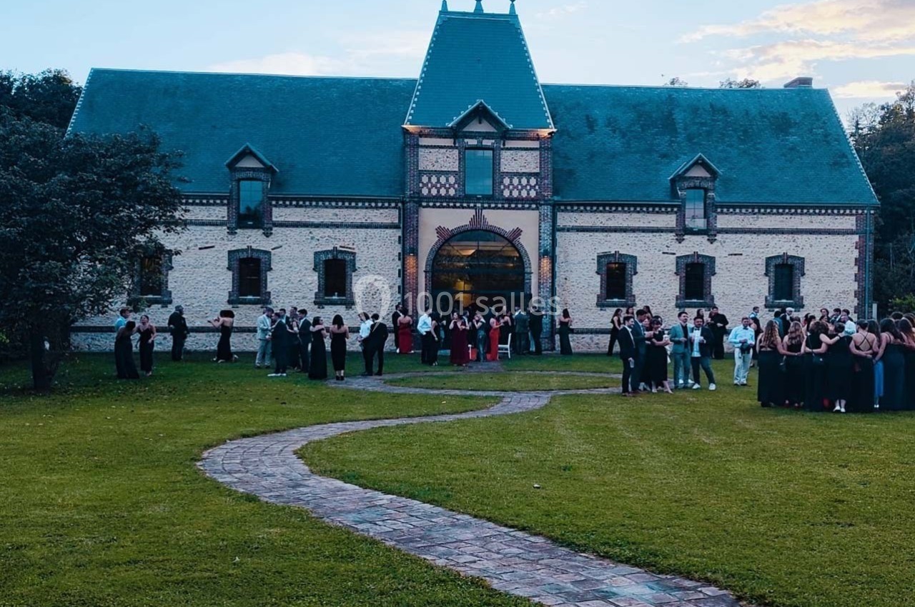 Location salle Sylvains-les-Moulins (Eure) - Domaine de Coulonge #29 Un groupe de personnes rassemblées devant un grand bâtiment en briques avec un toit en ardoise, entouré de pelouse.