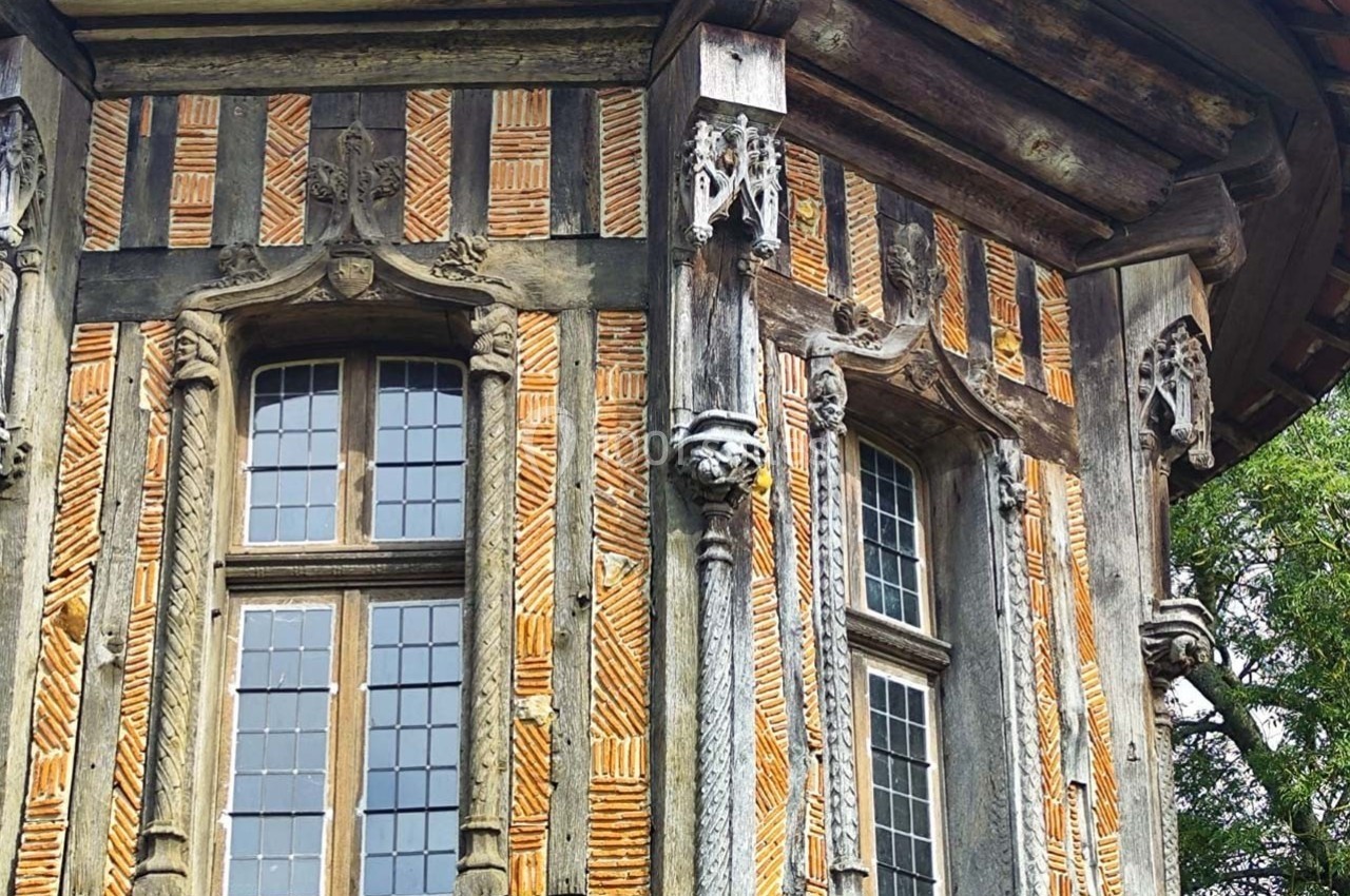 Location salle Sylvains-les-Moulins (Eure) - Domaine de Coulonge #48 Façade d'une maison à colombages avec des motifs en briques et des sculptures en bois autour des fenêtres.