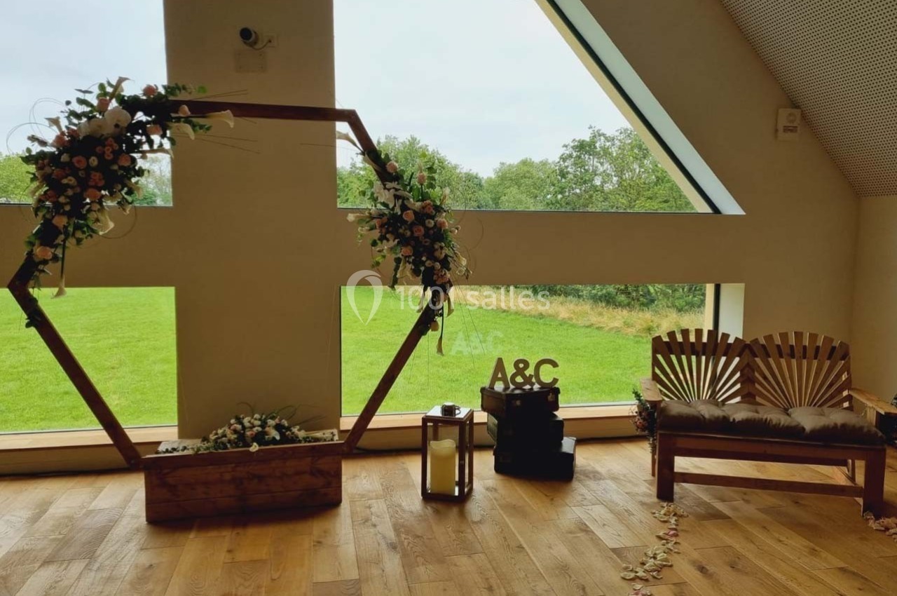 Location salle Sylvains-les-Moulins (Eure) - Domaine de Coulonge #39 Décoration de mariage avec arche hexagonale fleurie, banc en bois, lanterne et vue sur un jardin à travers une grande…