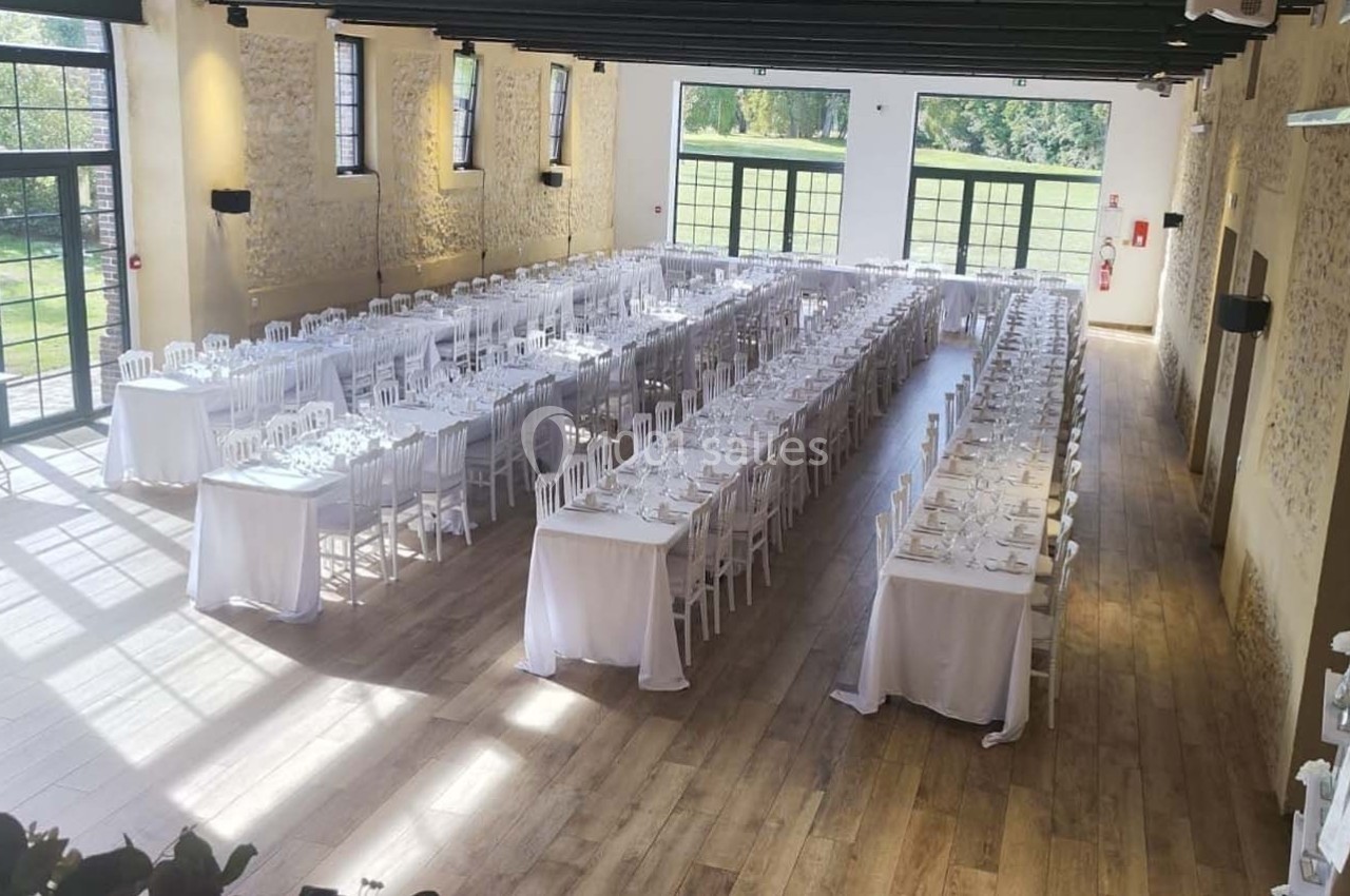 Location salle Sylvains-les-Moulins (Eure) - Domaine de Coulonge #13 Salle de réception lumineuse avec de longues tables dressées pour un événement, entourée de murs en pierre et grandes…
