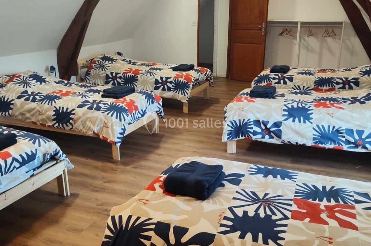 Location salle Sylvains-les-Moulins (Eure) - Domaine de Coulonge #47 Chambre mansardée avec six lits simples alignés, parure colorée et porte en bois au fond.