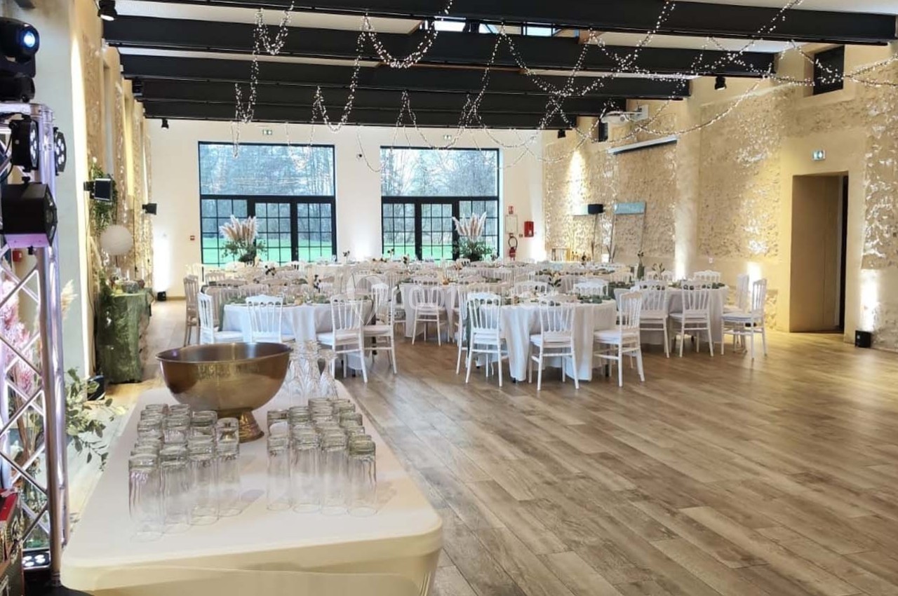 Location salle Sylvains-les-Moulins (Eure) - Domaine de Coulonge #5 Salle de réception lumineuse avec tables dressées, chaises blanches et décorations suspendues, vue sur un extérieur…