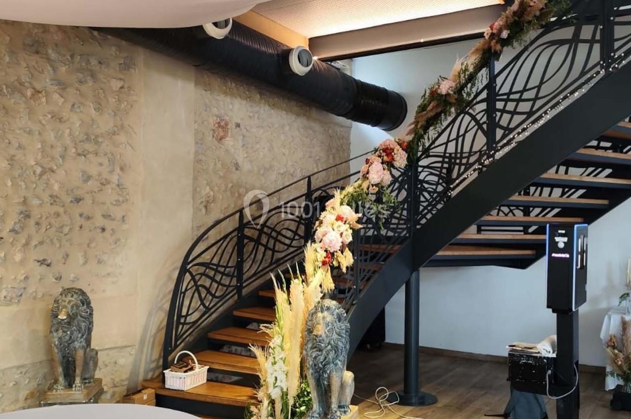 Location salle Sylvains-les-Moulins (Eure) - Domaine de Coulonge #49 Escalier en métal décoré de fleurs, situé dans un intérieur avec murs en pierre et table ornée à droite.