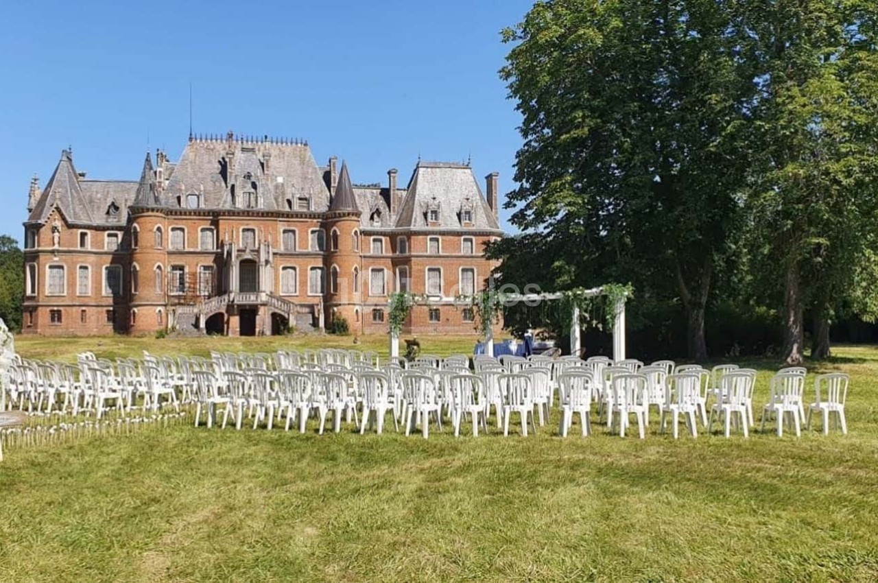 Chaises blanches disposées en extérieur devant un château en briques rouges entouré de verdure.