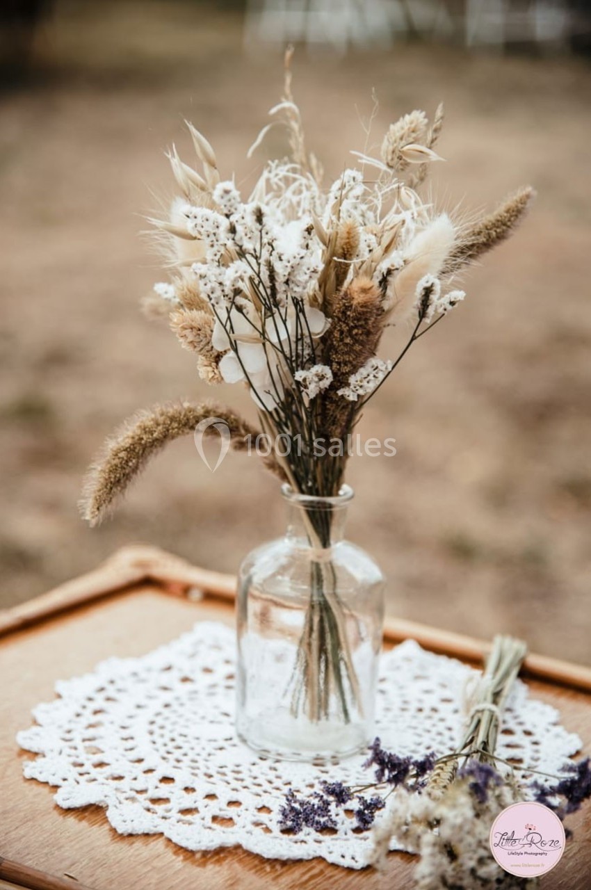 Location salle Sylvains-les-Moulins (Eure) - Domaine de Coulonge #35 Bouquet de fleurs séchées dans un vase en verre, posé sur une nappe en dentelle sur une table en bois.