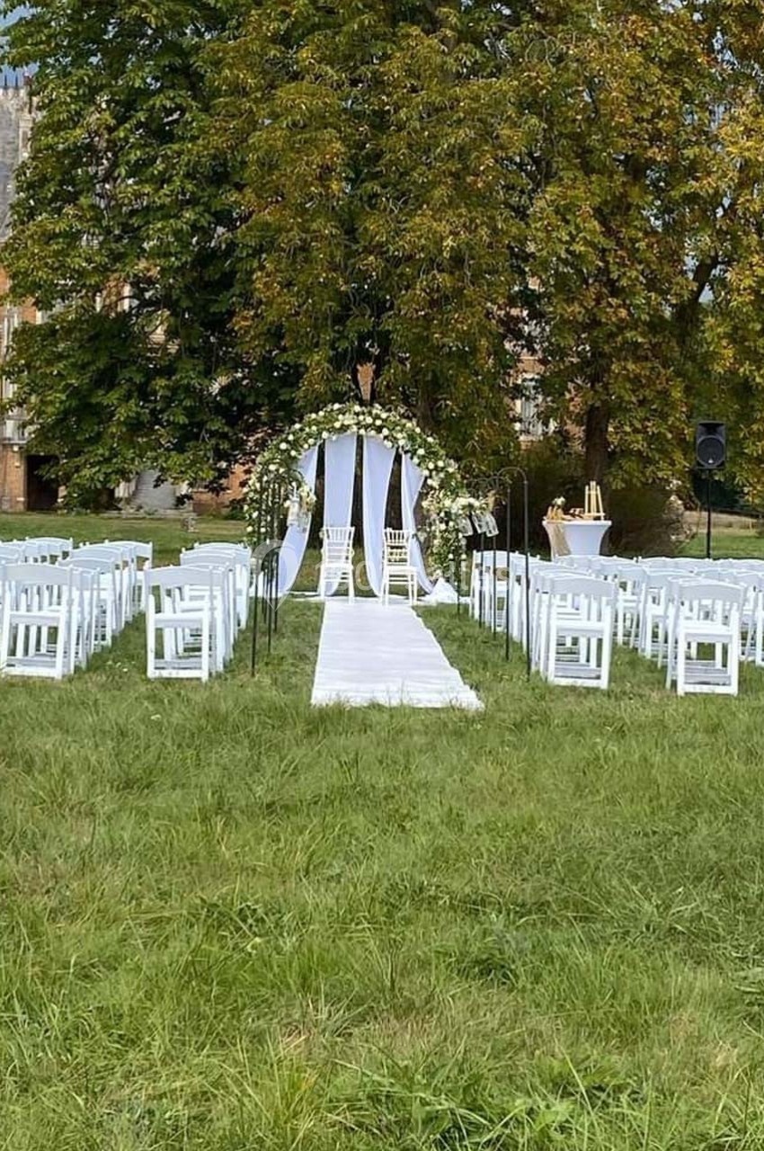 Location salle Sylvains-les-Moulins (Eure) - Domaine de Coulonge #26 Allée centrale bordée de chaises blanches menant à une arche fleurie pour une cérémonie en plein air.