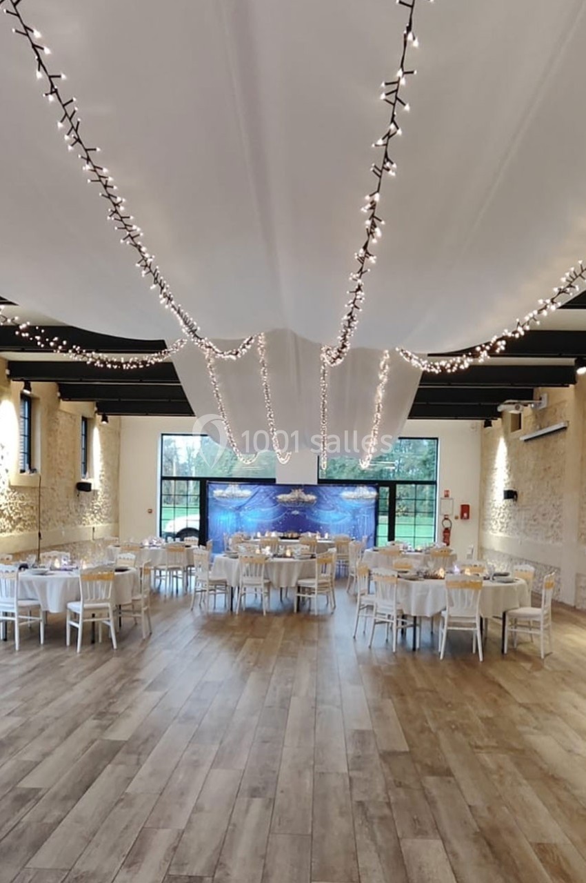 Location salle Sylvains-les-Moulins (Eure) - Domaine de Coulonge #8 Salle de réception lumineuse avec tables dressées, guirlandes lumineuses suspendues et vue sur un jardin à travers de…