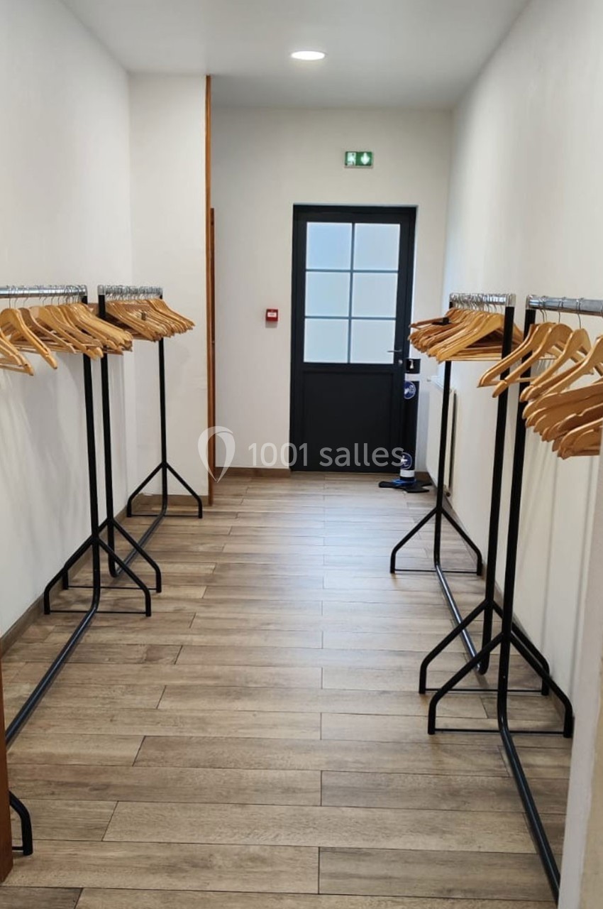 Location salle Sylvains-les-Moulins (Eure) - Domaine de Coulonge #55 Portant en métal noir avec cintres en bois alignés de chaque côté d'un couloir au sol en parquet clair.