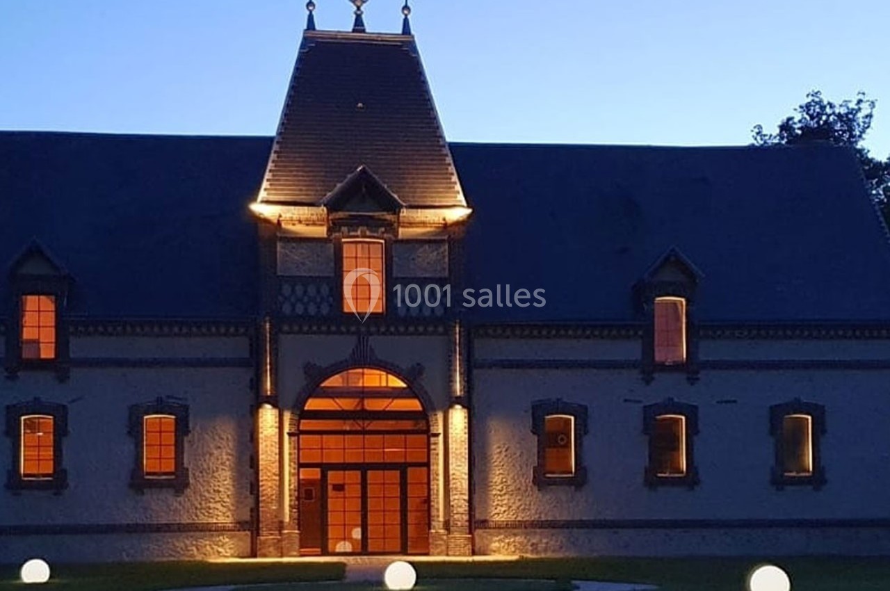 Location salle Sylvains-les-Moulins (Eure) - Domaine de Coulonge #32 Façade d'un bâtiment ancien éclairé à la tombée de la nuit, avec des lumières rondes sur la pelouse.