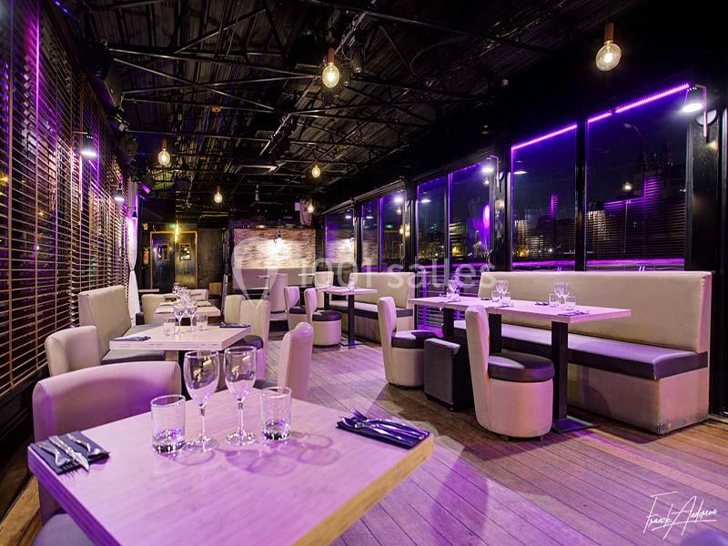 Salle de restaurant moderne avec tables dressées, éclairage violet et grandes baies vitrées donnant sur l'extérieur.