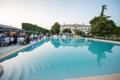 Miniature Location salle Lançon-Provence (Bouches-du-Rhône) - La Bastide d'Astres #6 Vue d'une terrasse avec parasols et piscine, encadrée par des haies sombres et un ciel dégagé en arrière-plan.