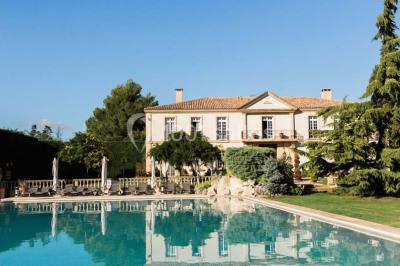 Miniature Location salle Lançon-Provence (Bouches-du-Rhône) - La Bastide d'Astres #9 Vue d'une terrasse avec parasols et piscine, encadrée par des haies sombres et un ciel dégagé en arrière-plan.