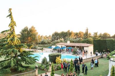 Miniature Location salle Lançon-Provence (Bouches-du-Rhône) - La Bastide d'Astres #10 Vue d'une terrasse avec parasols et piscine, encadrée par des haies sombres et un ciel dégagé en arrière-plan.