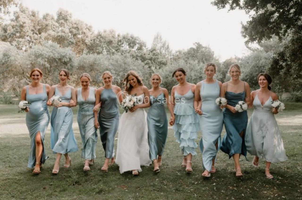 Un groupe de femmes en robes bleues et une en robe blanche marchant sur une pelouse dans un parc verdoyant.