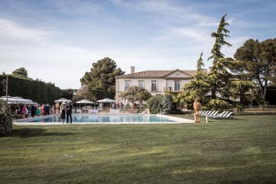 Miniature Location salle Lançon-Provence (Bouches-du-Rhône) - La Bastide d'Astres #16 Vue d'une terrasse avec parasols et piscine, encadrée par des haies sombres et un ciel dégagé en arrière-plan.