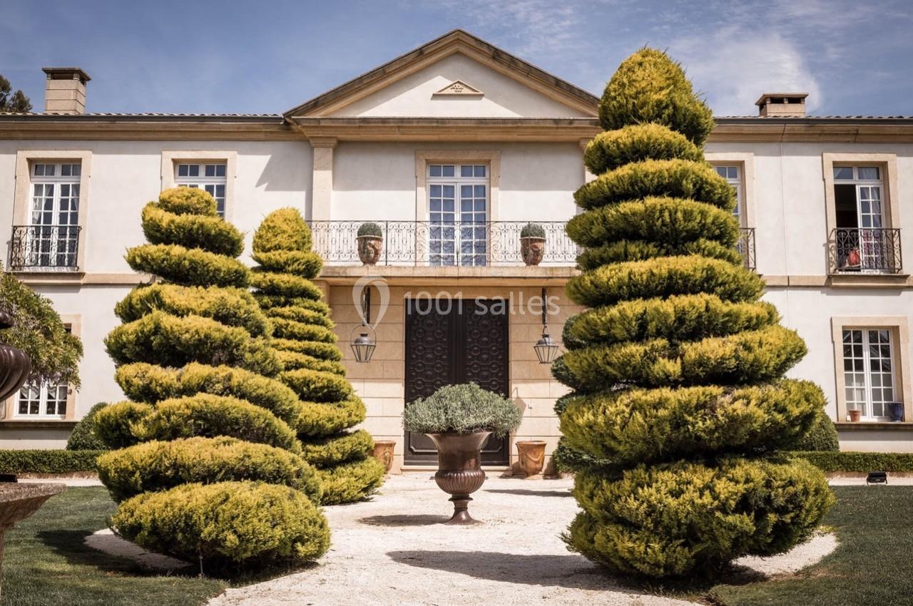 Façade d'une maison élégante entourée de buissons taillés en spirale et d'une allée gravillonnée.