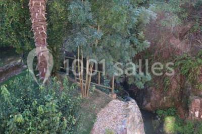 Petit ruisseau bordé de végétation avec des tentes blanches installées pour un événement en arrière-plan.