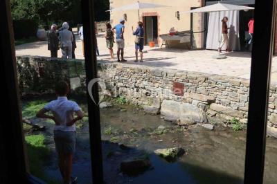 Petit ruisseau bordé de végétation avec des tentes blanches installées pour un événement en arrière-plan.