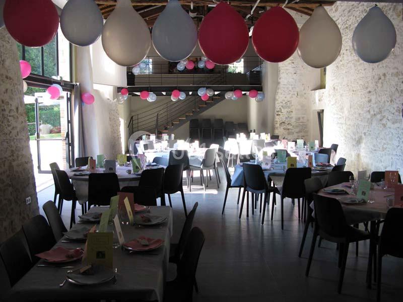 Salle décorée avec des ballons colorés et des tables dressées pour un événement festif.