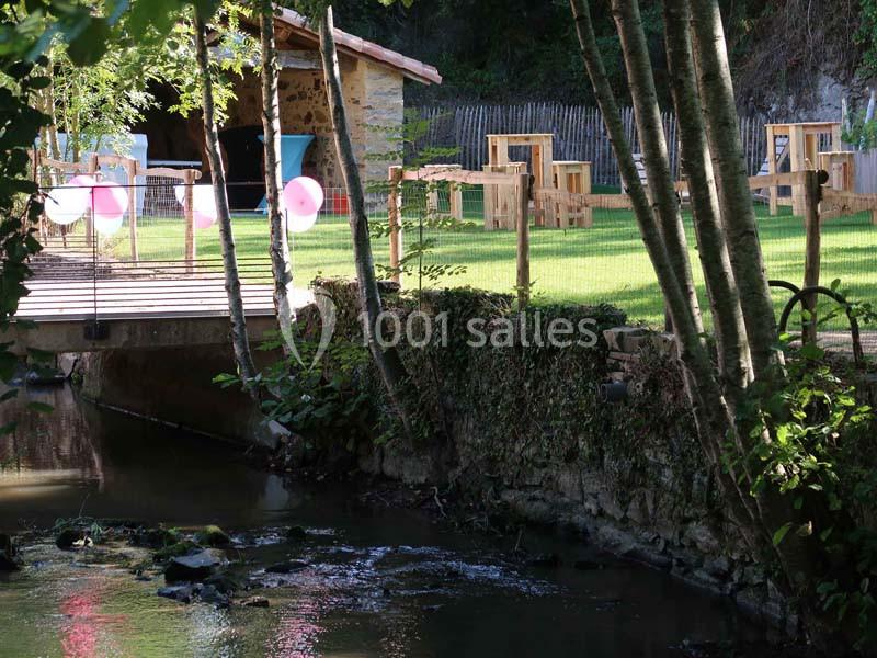 Petit pont en bois traversant un ruisseau, avec une terrasse aménagée et décorée de ballons roses en arrière-plan.