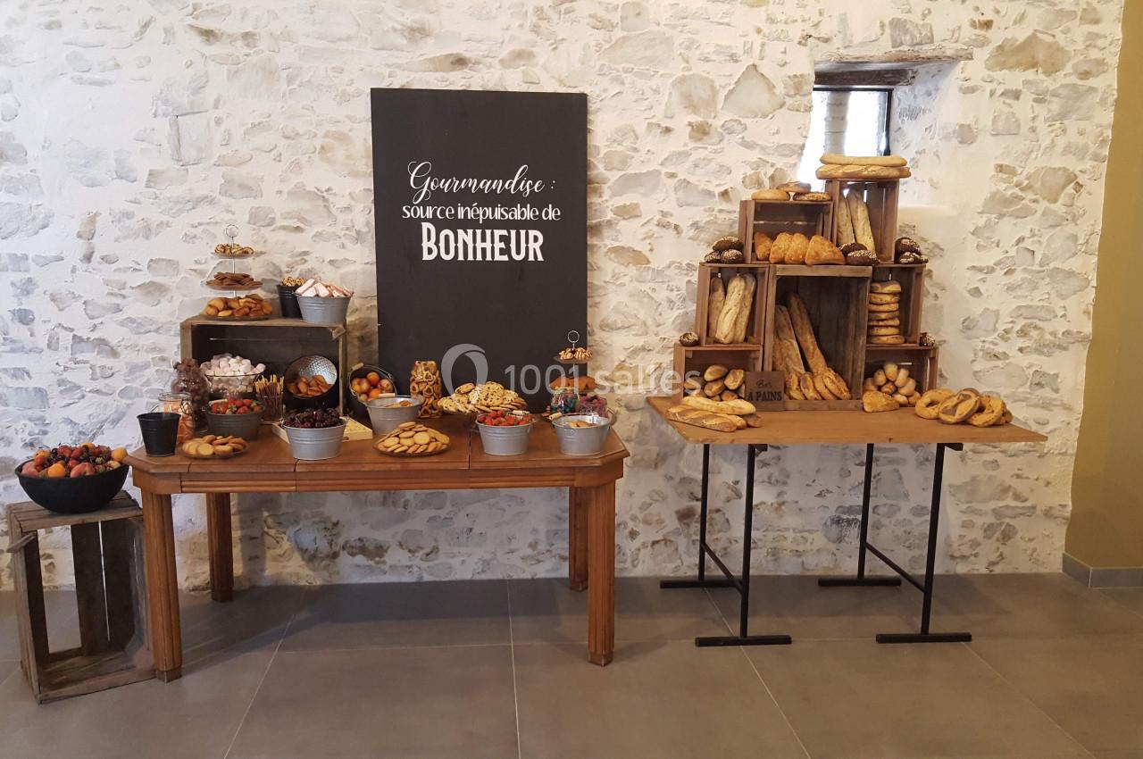 Buffet de pains et viennoiseries disposés sur des tables en bois devant un mur en pierre.