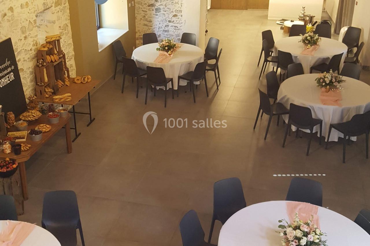 Salle de réception avec tables rondes décorées, chaises noires et buffet disposé sur une table en bois.