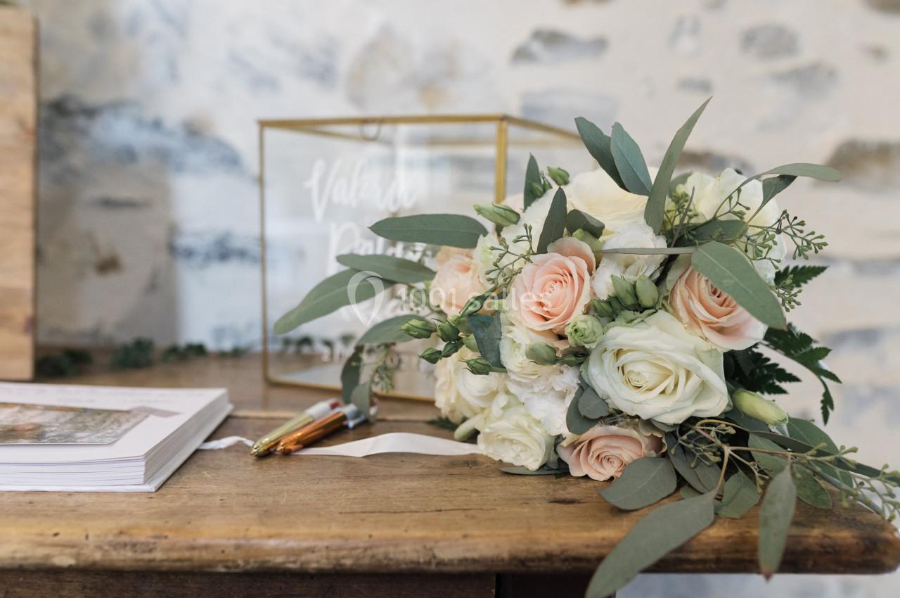 Bouquet de roses blanches et roses posé sur une table en bois près d'une boîte transparente et de documents.