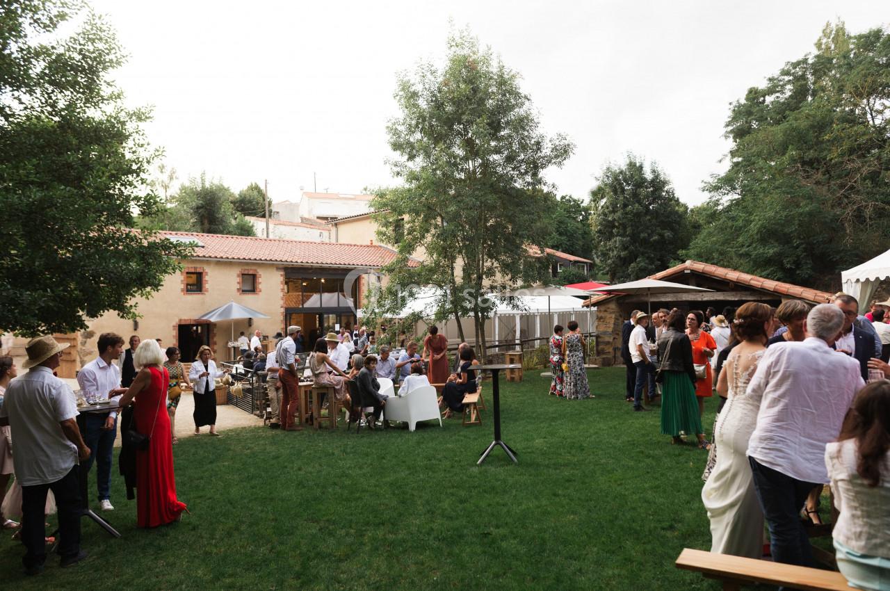 Personnes rassemblées dans un jardin pour un événement en plein air, entourées de bâtiments et de verdure.