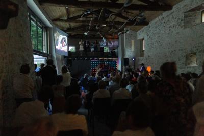 Petit ruisseau bordé de végétation avec des tentes blanches installées pour un événement en arrière-plan.